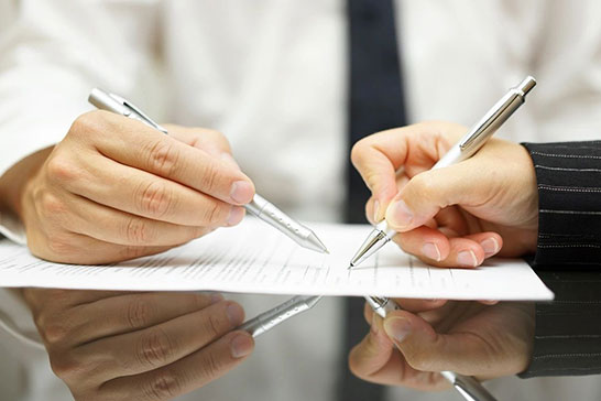 Two people are writing on a piece of paper.