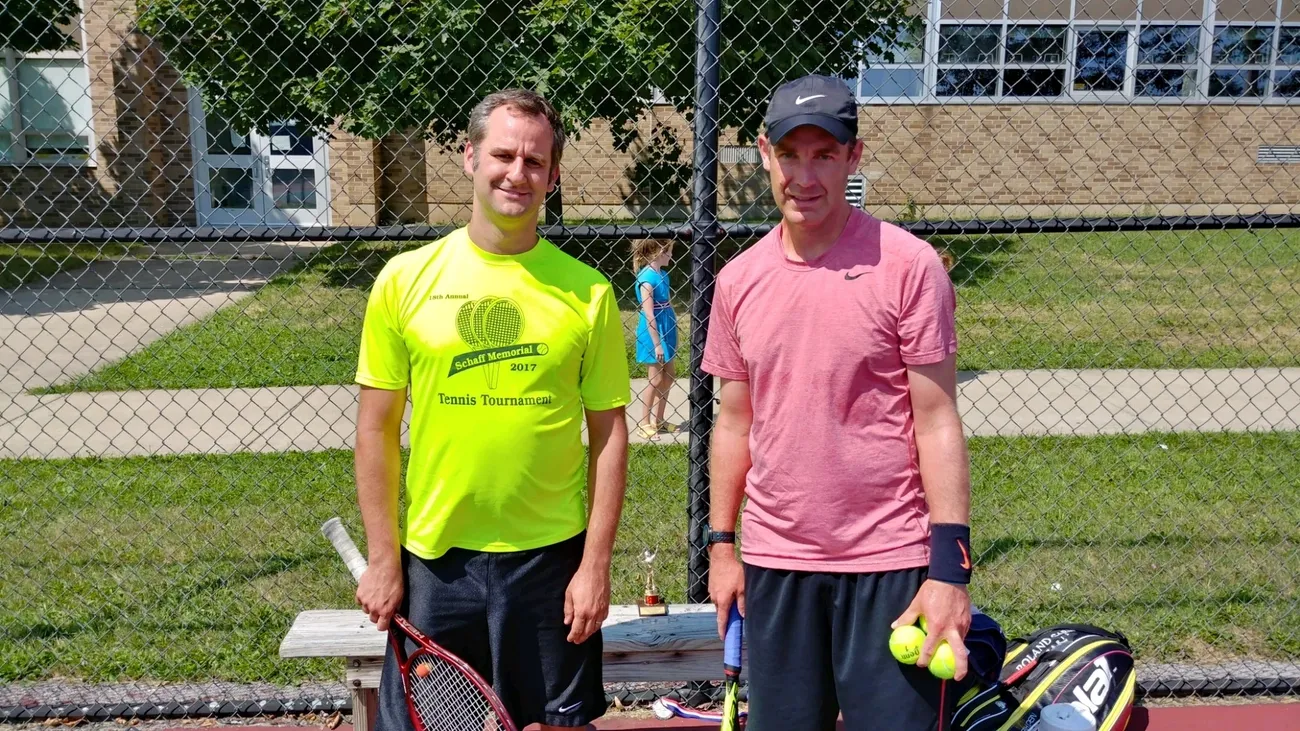 Two men standing next to each other holding tennis rackets.