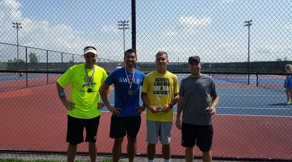 Four men standing on a tennis court holding medals.