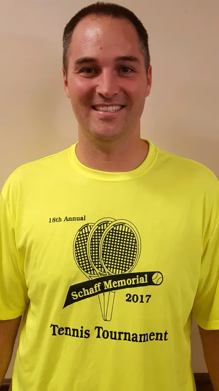 A man wearing a yellow shirt with tennis rackets on it.