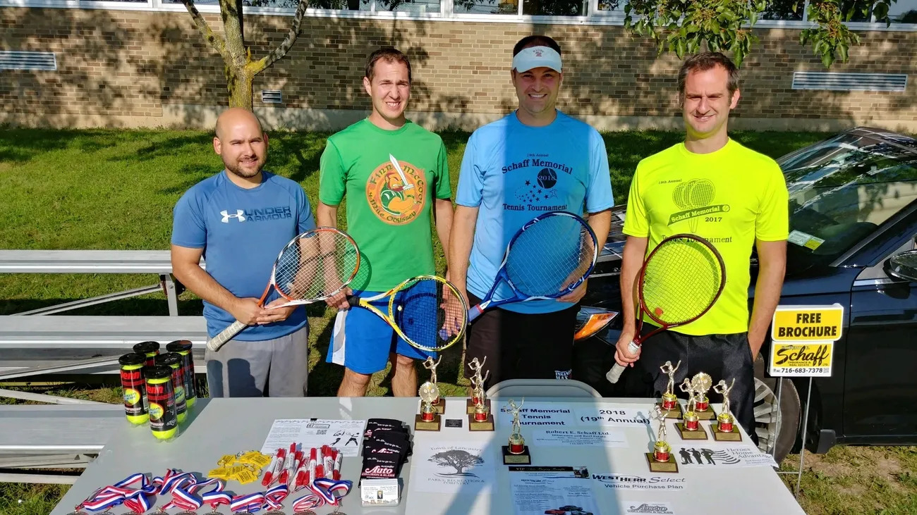 Four men holding tennis rackets and a table with trophies.