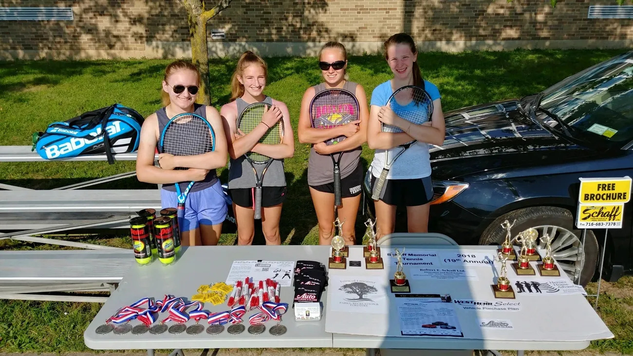 Four girls standing next to a table with tennis rackets.