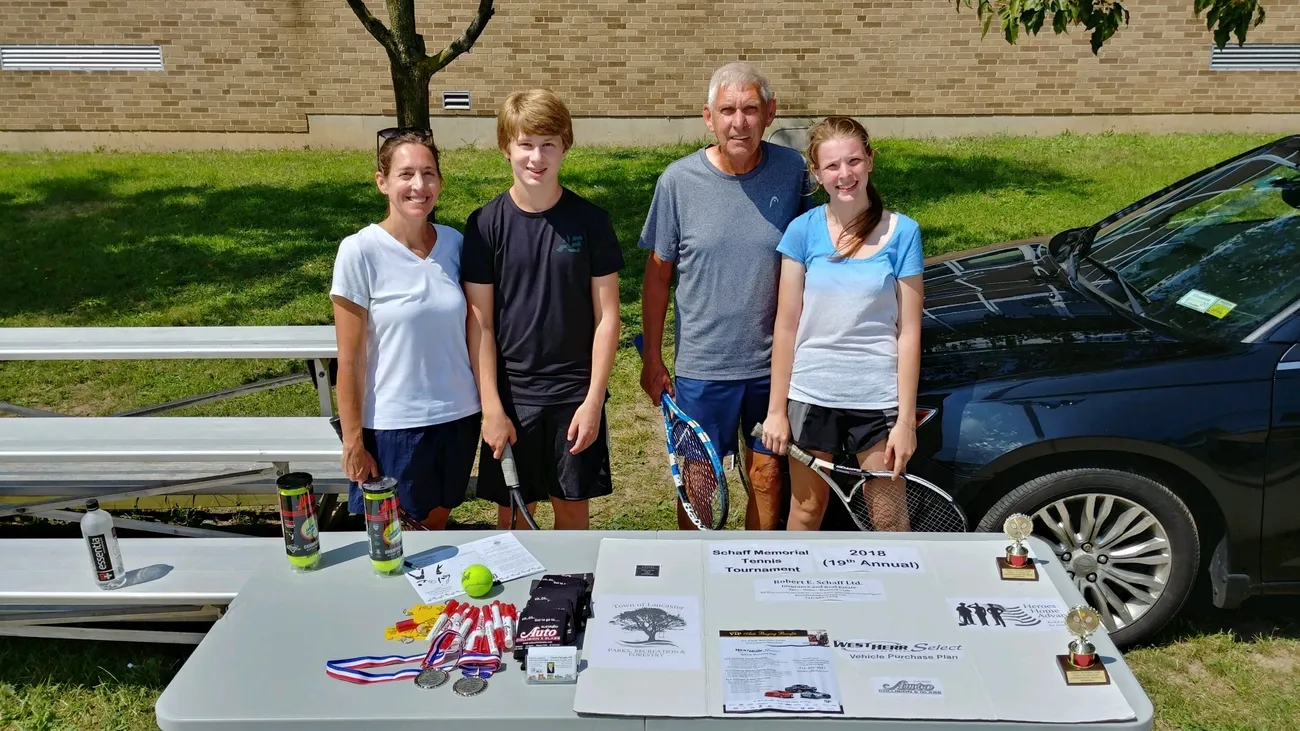 A family standing in front of a table with tennis equipment.